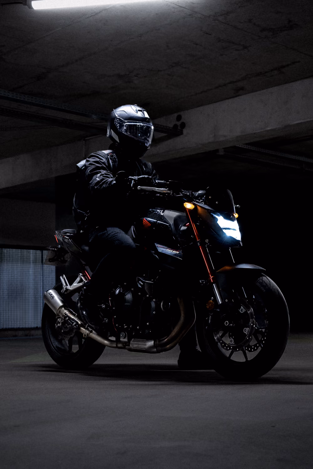 Gros plan d'une moto Honda noire avec phare allumé dans un parking souterrain, par Tony Delage